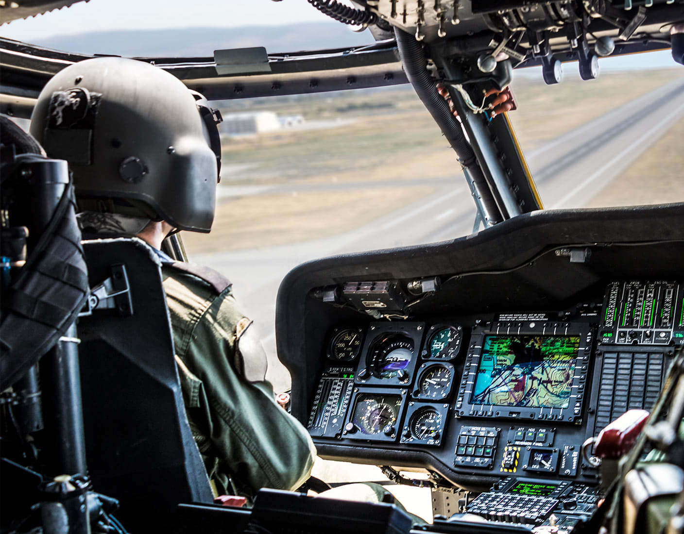 A pilot operating a helicopter, focused on a computer screen displaying flight data and navigation information.